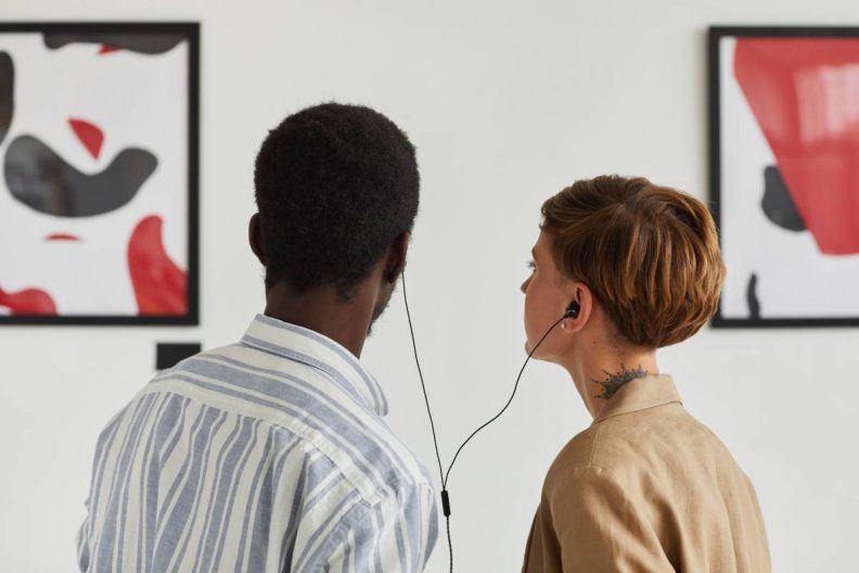 Ein Paar steht in einem Museum vor einem Bild und teilt sich Kopfhörer