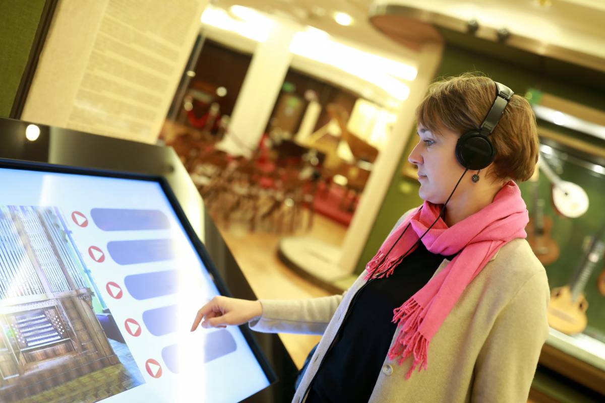 A woman with headphones stands in front of a large touchscreen in a museum