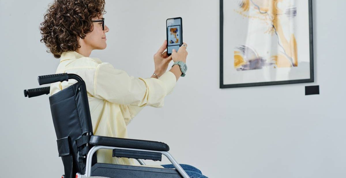 A woman in a wheelchair in front of a picture in a museum, holding her phone
